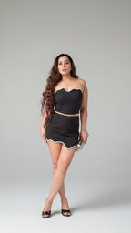 Woman wearing a black outfit with a strapless top and skirt on a gray background