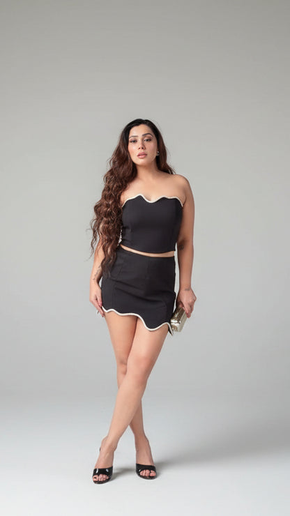 Woman wearing a black outfit with a strapless top and skirt on a gray background